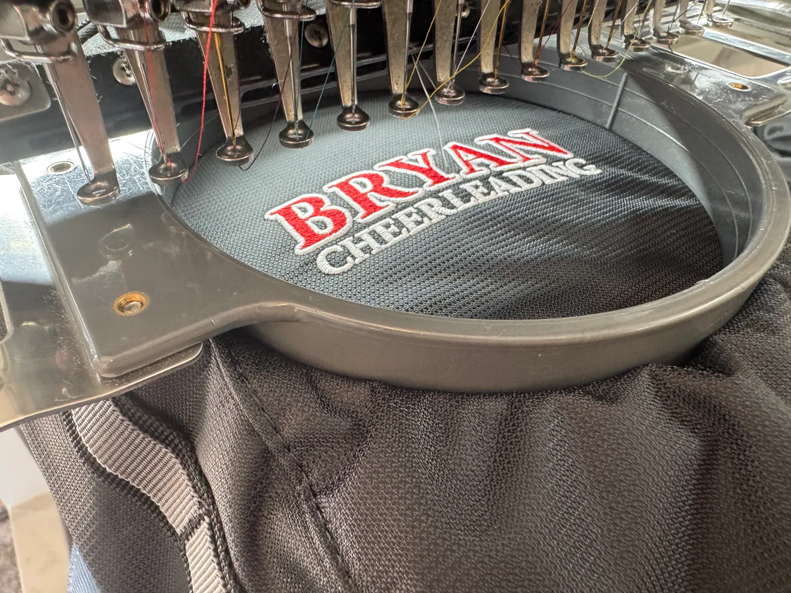 BRYAN CHEERLEADING embroidered in red and white thread on black mesh, still in the machine hoop
