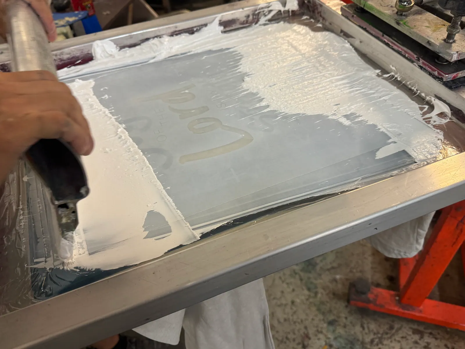 Hand spreading white ink across a screen on the screen printing press