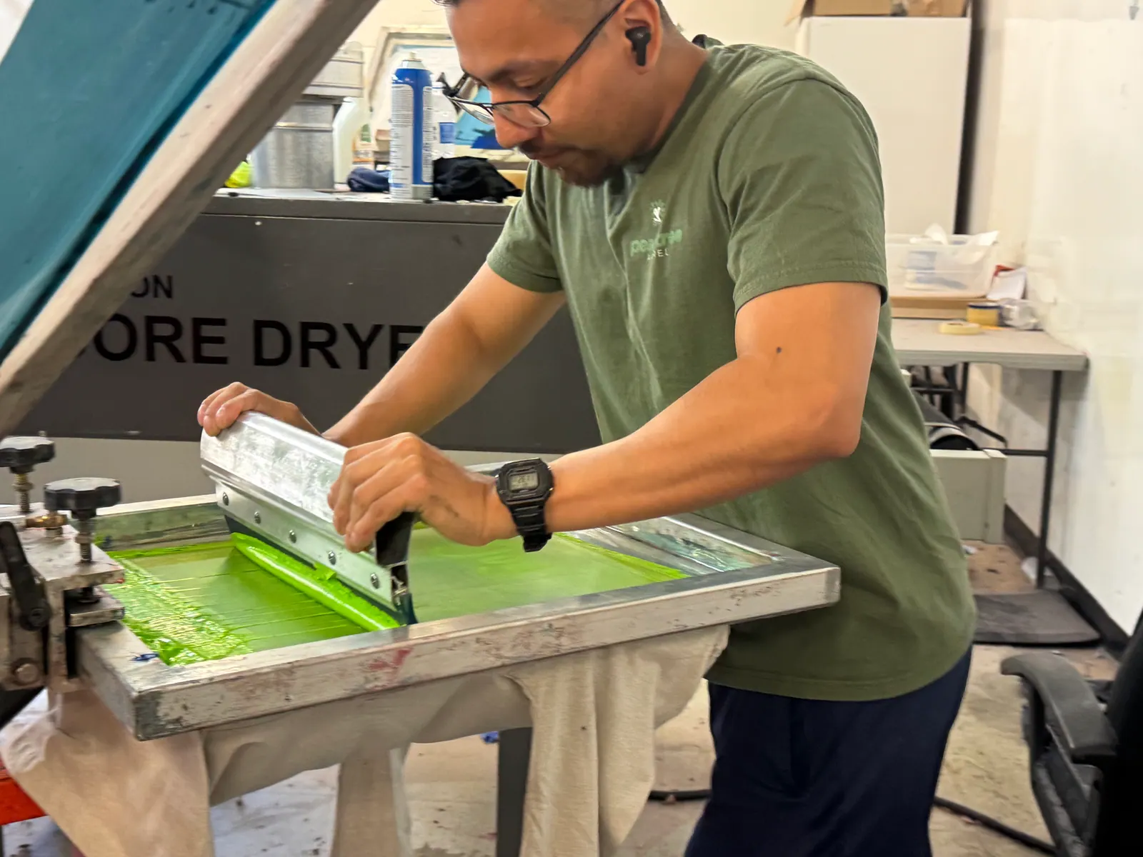Screen printer pulling a squeegee through bright green ink on a press screen