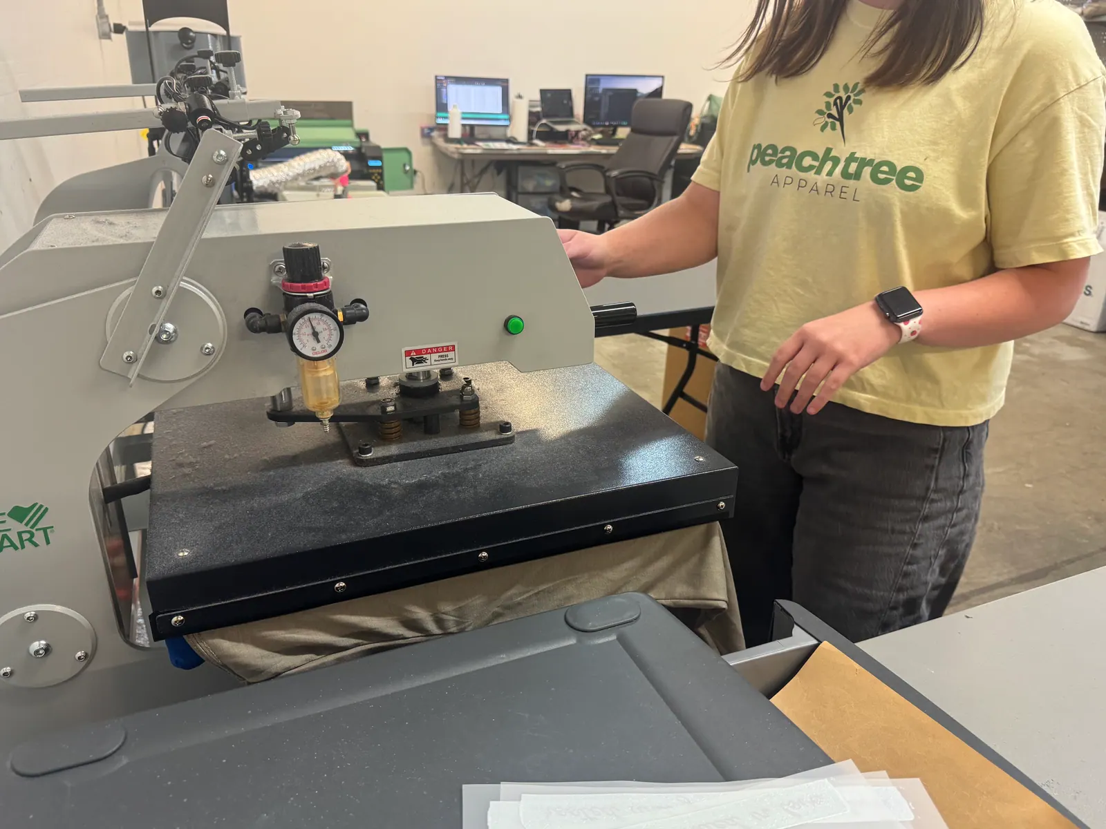 Team member in a yellow PeachTree Apparel logo T-shirt working at the heat press