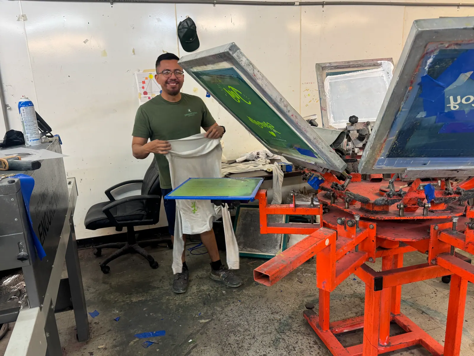 Smiling screen printer in a PeachTree Apparel shirt holding a T-shirt at the carousel press